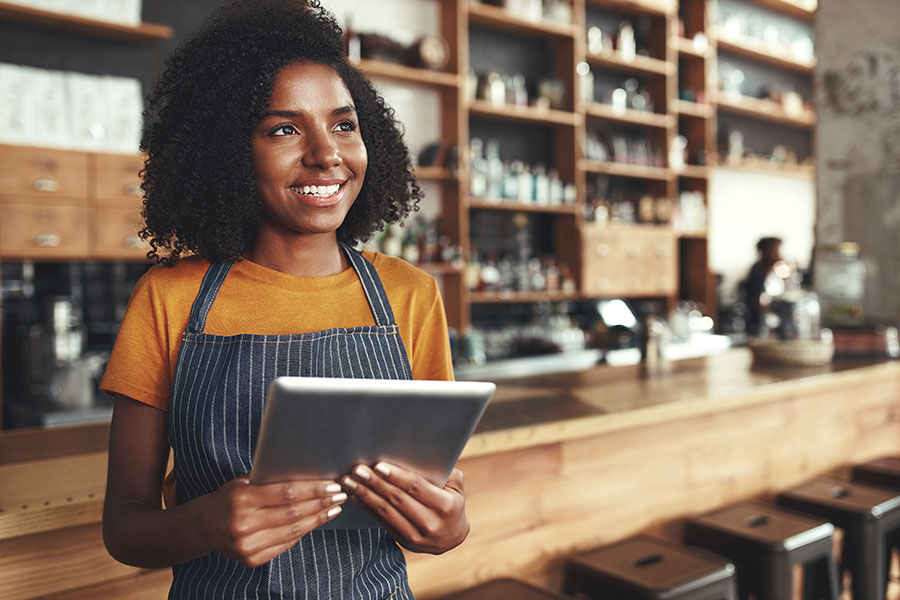 Business Insurance - Smiling Young Business Owner Standing In Her Store While Holding Tablet